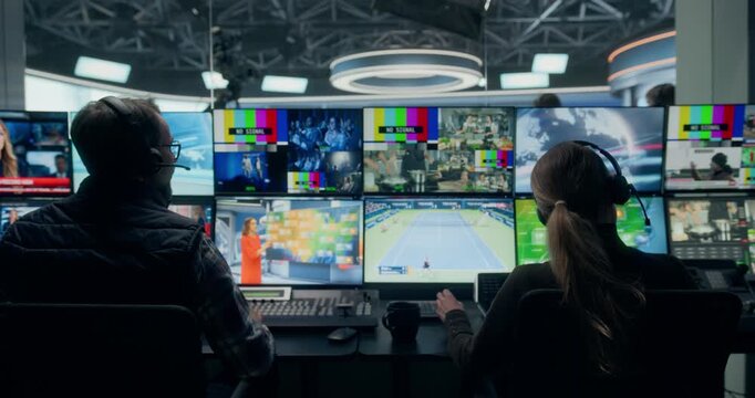 Backstage TV Station Production Control Room Manages a Live News Channel as Technicians Monitor Multiview Screens, Feeds, Coordinate Broadcasts. Camera Elevate Zoom into News Studio with Presenter