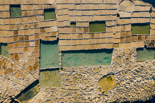 Aerial view of an intricate patchwork of salt pans reflecting the sky, creating a mosaic of textures and tones, Zebbug, Malta.