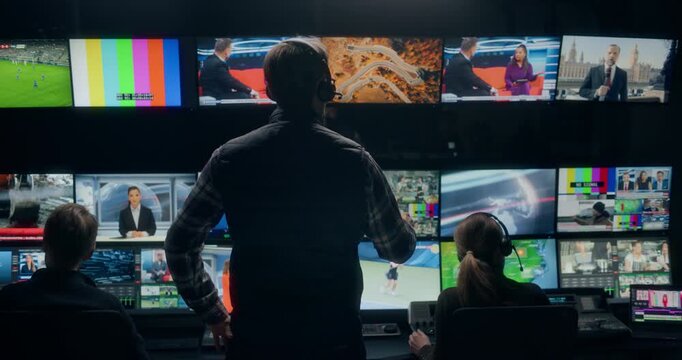 Backstage TV Station Production Control Room Captures Technicians and Operators Directing Live News Broadcasting, Switching Anchor, Weather and Sport Channel Feeds Across Monitor Walls and Consoles.