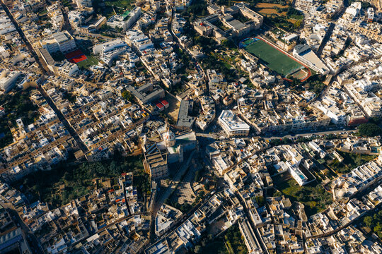 Aerial view of the intricate maze of sun-drenched buildings, with a contrasting green field, Ir-Rabat, Mdina, Malta.