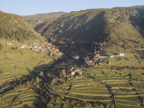 Aerial view of a quaint village nestled in terraced fields under the watchful gaze of rugged mountains, Sistelo, Viana do Castelo, Portugal.