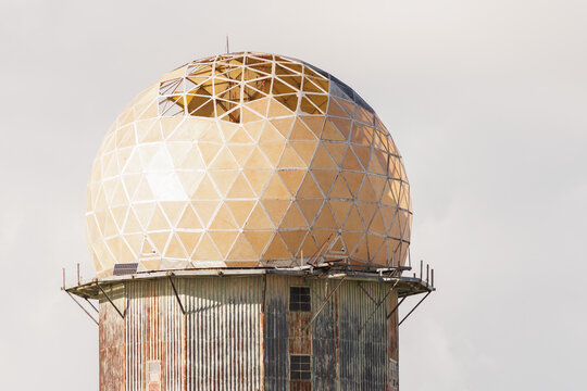 Detailed view of a weathered and broken geodesic radar dome structure with missing panels against a clear sky. Stock photo