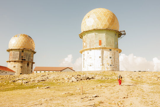Tourist walking near abandoned radar station domes on top of a rocky mountain peak during a sunny day. Stock photo