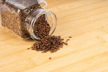 Close-up of golden brown flax seeds spilling abundantly from a clear glass jar onto a warm, rustic wooden surface, highlighting natural health and omega-3 nutrition.