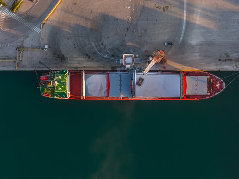 Aerial view of a vibrant red and white cargo ship nestled against the stark concrete of the port, reflecting in the deep turquoise waters, Vasto, Abruzzo, Italy.