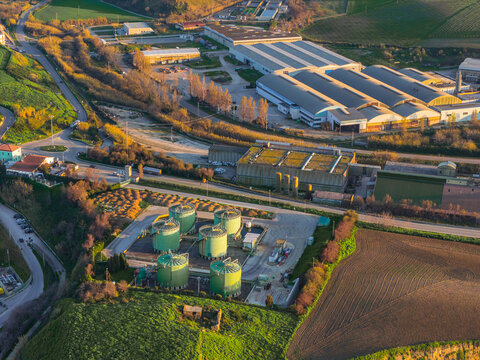 Aerial view of industrial buildings and tanks nestled amidst the green and brown fields, a stark contrast of human construction and natural landscapes, Vasto, Abruzzo, Italy.
