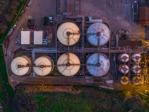 Aerial view of industrial tanks gleaming under the twilight sky, a symphony of metallic hues and geometric precision, casting long shadows across the landscape, Vasto, Abruzzo, Italy.