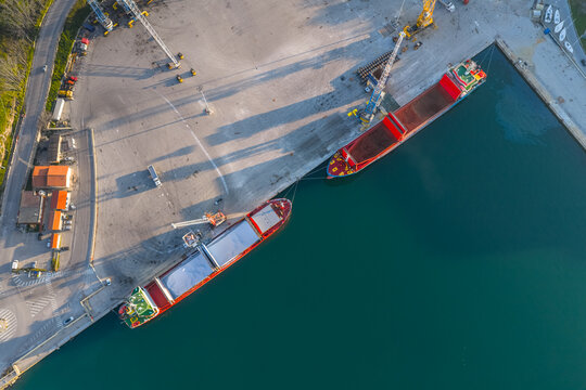 Aerial view of cargo ships docked along the concrete pier, contrasting with the deep teal water, Vasto, Abruzzo, Italy.