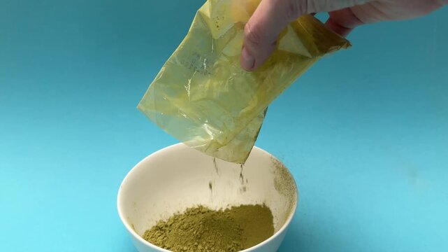 Female hands pour henna and indigo basma powder into white bowl for hair dye preparation closeup