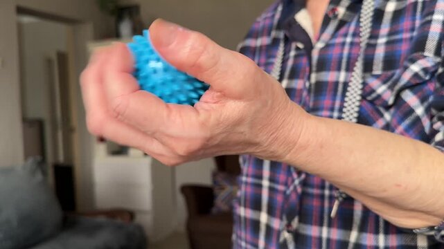 Senior woman squeezes massage ball for hand rehabilitation closeup