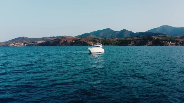 Large White Yacht on Blue Sea with Rocky Hills and Coastal Village in Background