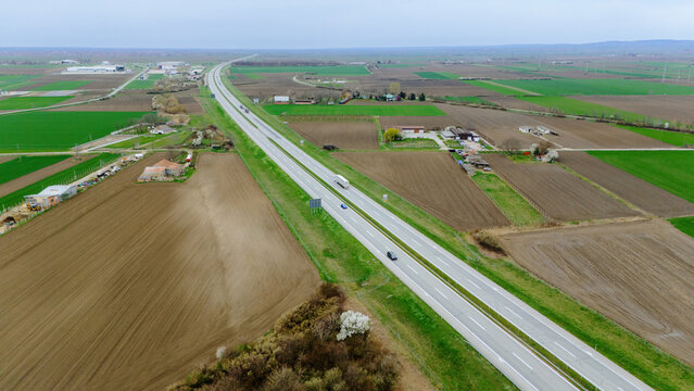 Aerial view of a modern highway cutting through a patchwork of vibrant green and earthy brown fields under a vast sky, Sremska Mitrovica, Vojvodina, Serbia.