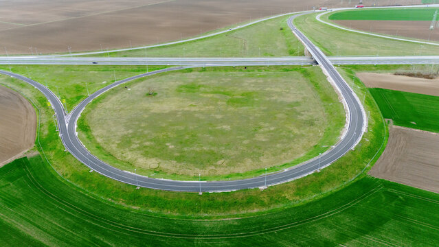 Aerial view of curving roads cutting through vibrant green fields and tilled earth, a tapestry of nature and infrastructure, Sremska Mitrovica, Vojvodina, Serbia.