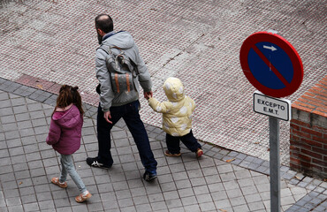 Padre con sus hijos pequeños de la mano acompañando camino del colegio