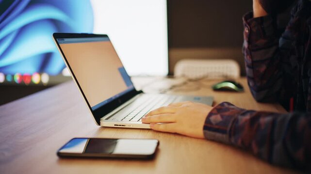 Person working on laptop at desk with smartphone and modern lighting setup in background