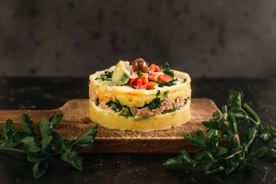 A dish called Causa rellena with ingredients such as tuna and avocado with parsley leaves on the sides.
