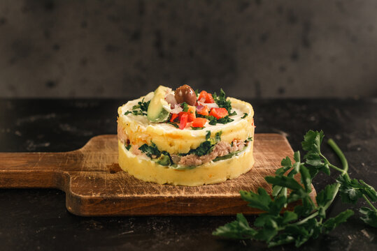 Peruvian dish called Causa rellena presented on a wooden board next to a sprig of parsley.