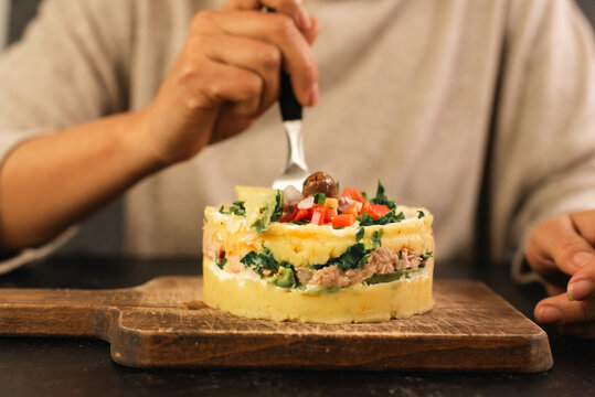 Unrecognizable person cutting a piece of Causa rellena with a fork.