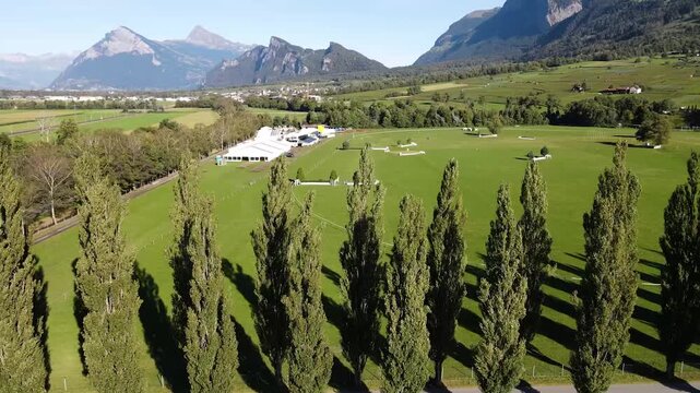 Drone tracks parallel to tree lined road overlooking equestrian grounds.