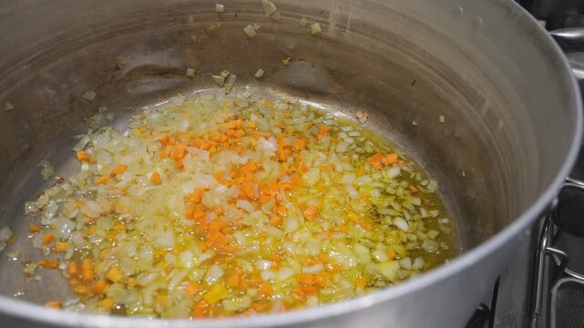 Close-up view of finely chopped onions and carrots sizzling in hot oil within a large pot, preparing for a traditional African dish
