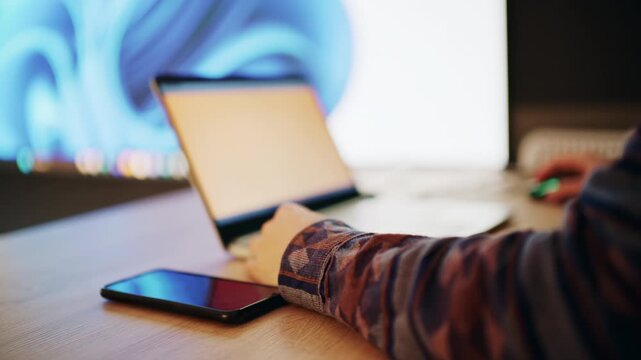 Person working on laptop at desk with smartphone and modern lighting setup in background