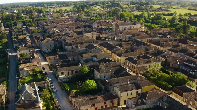 Historic stone town of Monpazier surrounded by the green valley landscape of the Dordogne region. Wide aerial drone perspective.