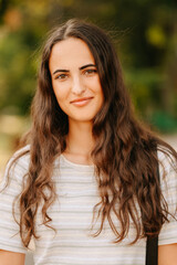 Obraz premium Closeup Smiling Caucasian Woman With Wavy Hair, Warm Sunlight And Blurred Green Background, Casual Striped