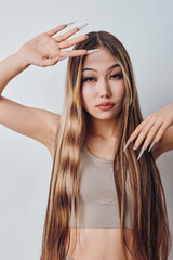 Naklejka premium Young woman with long straight hair and natural makeup posing with hands near face in studio. Casual clothing and smooth skin with neutral expression on light background.