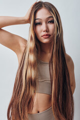 Obraz premium Young woman with long straight hair wearing beige crop top posing in studio. Beauty portrait with natural makeup, confident expression and soft lighting on white background.