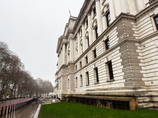 Naklejka premium Neoclassical His Majesty's Treasury government building with columns and wet street in London, UK on an overcast day
