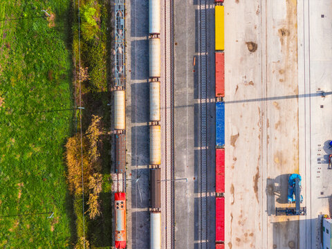 Aerial view of trains with colorful containers contrasting against the green fields and concrete, creating a striking industrial landscape, Atessa, Abruzzo, Italy.