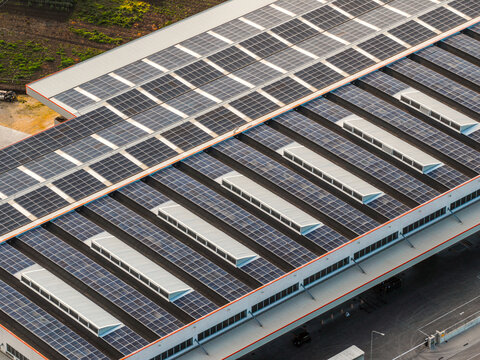 Aerial view of a rooftop covered in solar panels glinting under the sun, interspersed with skylights, creating a geometric tapestry of light and shadow, Atessa, Abruzzo, Italy.