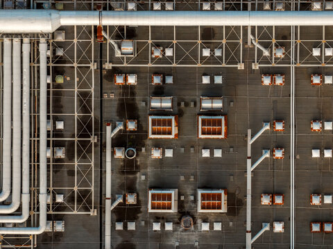 Aerial view of a complex industrial rooftop with interconnected pipes and vents casting shadows on the flat surface, Atessa, Abruzzo, Italy.