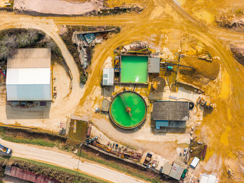 Aerial view of industrial buildings contrasting with bright green pools amidst the stark, earthy landscape, Atessa, Abruzzo, Italy.