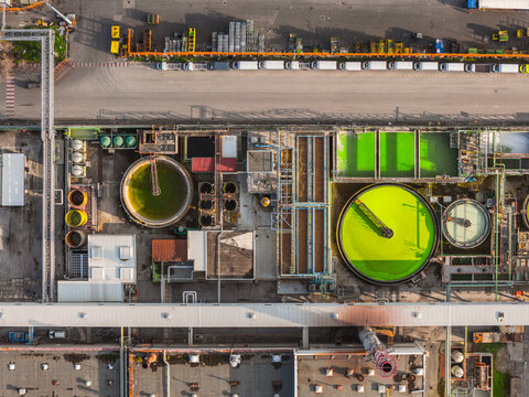 Aerial view of wastewater treatment plant showing circular clarifiers filled with vibrant green algae contrasting against the industrial landscape, Atessa, Abruzzo, Italy.