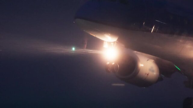 Commercial airplane taking off at night or dusk, accelerating down the runway with bright landing lights, engine glow, and exhaust vapor during snow blizzard
