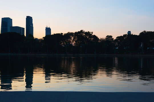 Bangkok cityscape silhouette reflecting on lake water during sunset at Benjakitti Park.