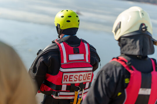 Rear view of professional emergency responders in safety gear and helmets overlooking an ice rescue operation, team coordination and winter emergency response concept