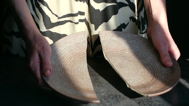 Dramatic shot of woman hands holding ceramic plate that breaks in half, symbolizing conflict, separation, divorce, broken relationships between people. Woman hands holding broken ceramic plate