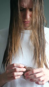 Upset young woman holding clump of fallen hair in hands, showing concern and sadness about alopecia thinning hormonal imbalance, representing common beauty, health problem. Hair loss concept. Vertical