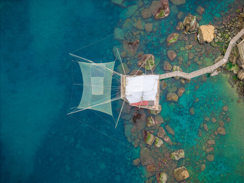 Aerial view of turquoise waters embracing the rocky coast with a Trabucco fishing structure standing proudly, San Vito Chietino, Abruzzo, Italy.