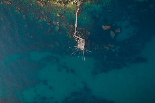 Aerial view of a traditional trabucco fishing structure stands in stark contrast to the turquoise sea and rocky shoreline, San Vito Chietino, Abruzzo, Italy.