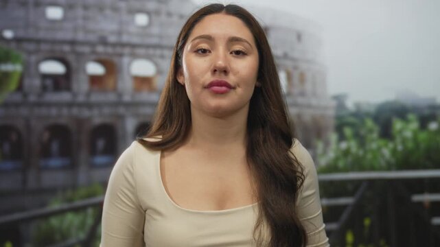 Young hispanic woman framing loser l gesture with her fingers at the roman coliseum building in daylight; mockery.
