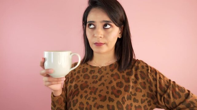 Close up of confused thoughtful pondering young Asian woman lady holding coffee cup thinks ideas choice doubt feels confusion, isolated over light pink studio background.