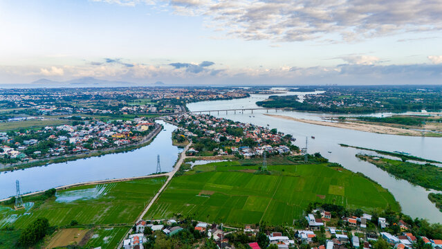 Aerial view of the winding river snaking through lush green rice paddies, connecting vibrant towns under a vast sky, Hoi An, Quang Nam, Vietnam.