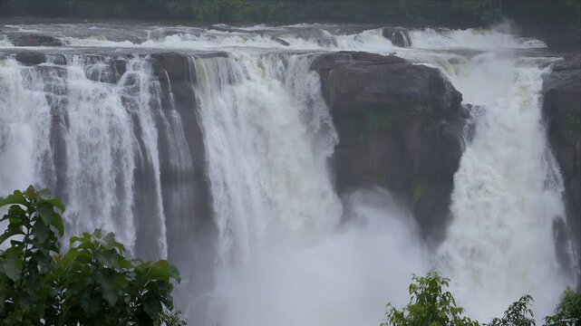 slow motion video of water fall rushing water over dark rocks. White foam crashes against stone with force and energy. Nature's raw power fills the frame. Ideal for backgrounds showing energy, Kerala