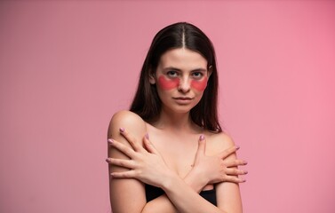 Fototapeta premium Woman posing with hydrating pink eye patches under her eyes, showcasing a relaxing beauty treatment and healthy skincare regimen for anti-aging and facial care