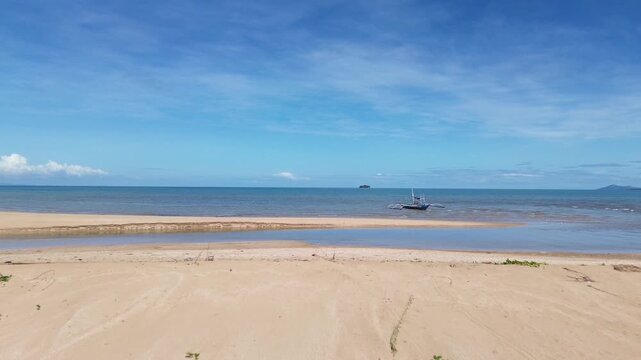 Cinematic aerial drone footage of small fishing boat resting on sandy tropical shoreline near Carles Iloilo Philippines traditional coastal fishing scene with calm ocean water on a sunny day.