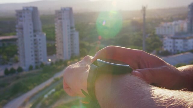 Close-up of a man adjusting settings on a smartwatch. Warm sunset light creates sun flares on the screen, with a blurred city background adding a modern urban lifestyle mood.