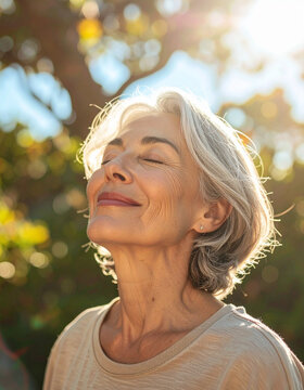 Authentic senior woman with eyes closed enjoying nature and direct sunlight conceptualizing freedom, healthy lifestyle, vitality, and the pure joy of living in the moment at any age
